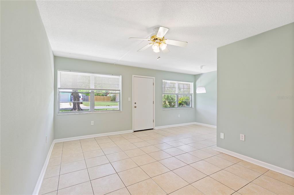 A bright room features light green walls, beige tile flooring, a ceiling fan, and windows — 1051 79TH AVENUE N UNIT 103, ST PETERSBURG, FL