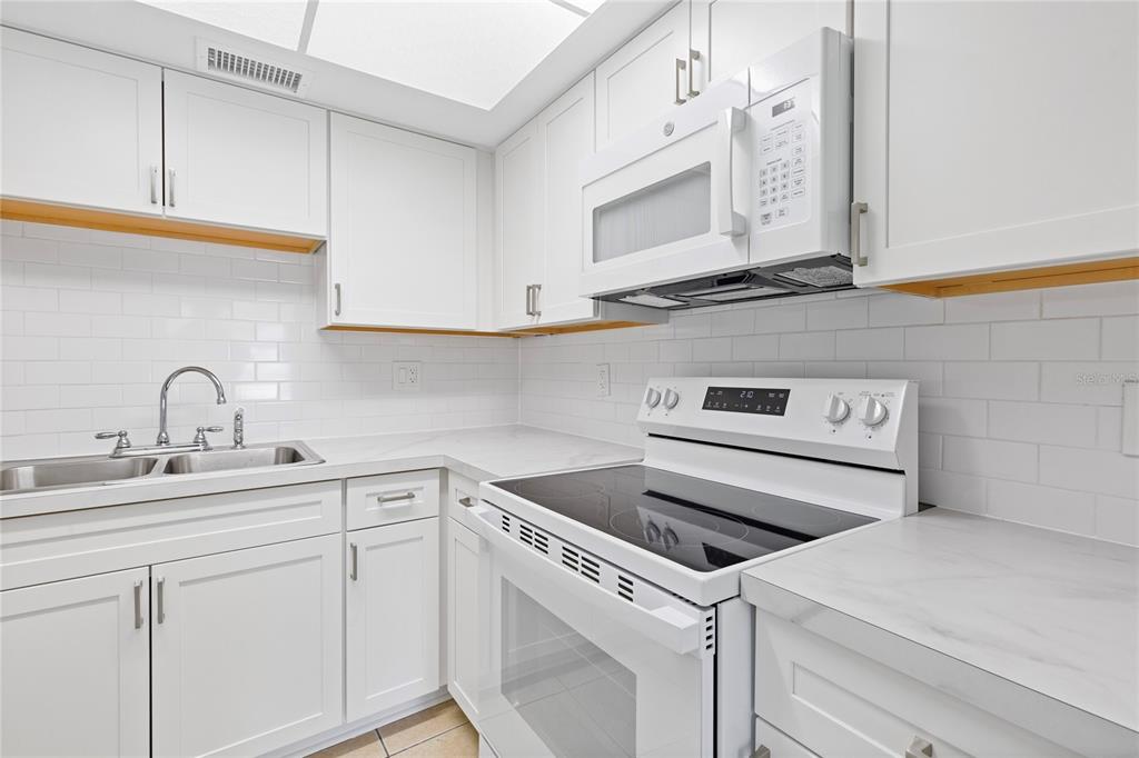A white kitchen features subway tile backsplashes, light countertops, and stainless steel appliances — 1051 79TH AVENUE N UNIT 103, ST PETERSBURG, FL