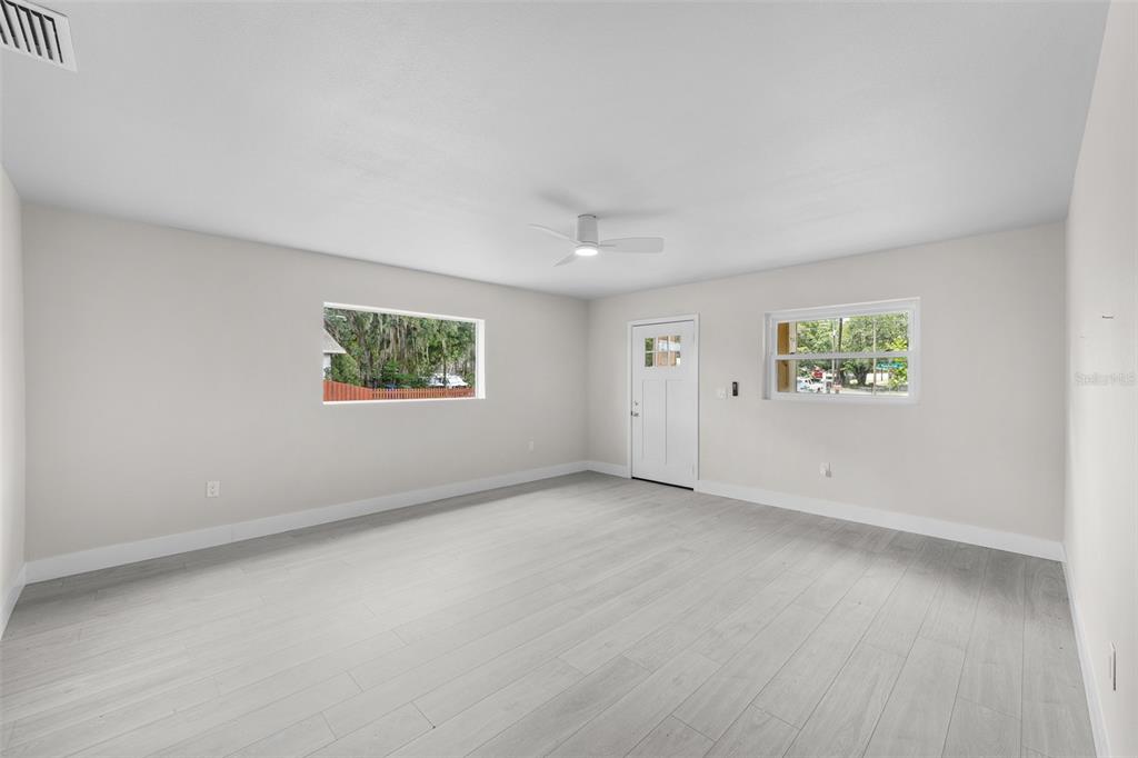A bright, empty room features light wood-look flooring, white walls, a ceiling fan, and two windows — 2001 E POWHATAN AVENUE, TAMPA, FL