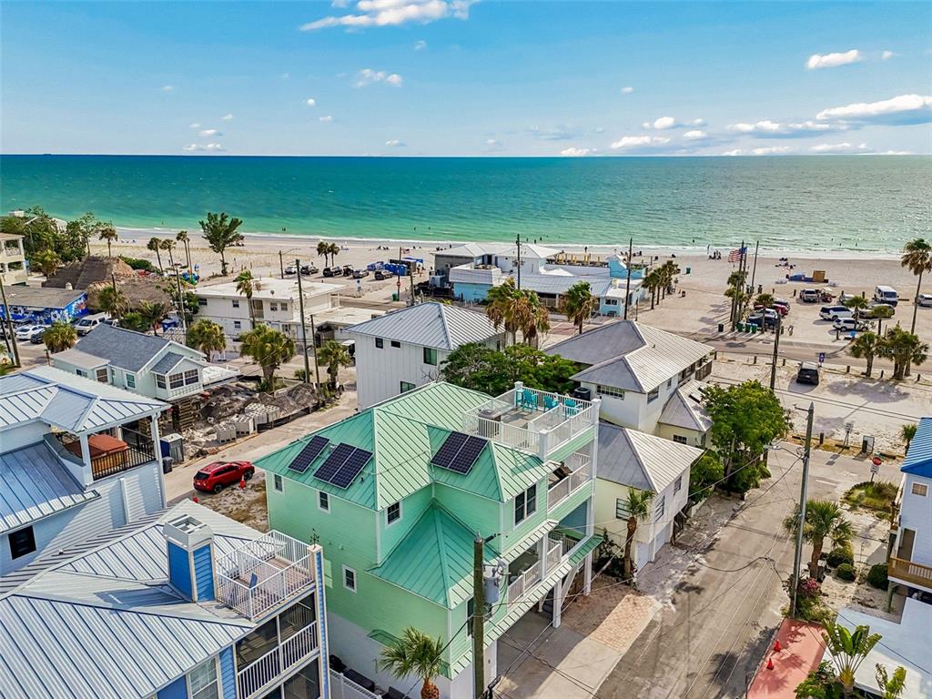 An aerial view shows a light green house with solar panels near a sandy beach — 111 91ST AVENUE, TREASURE ISLAND, FL