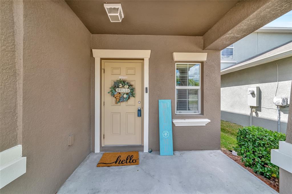 A covered front porch features a tan door with a wreath and a welcome mat — 17009 PEACEFUL VALLEY DRIVE, WIMAUMA, FL