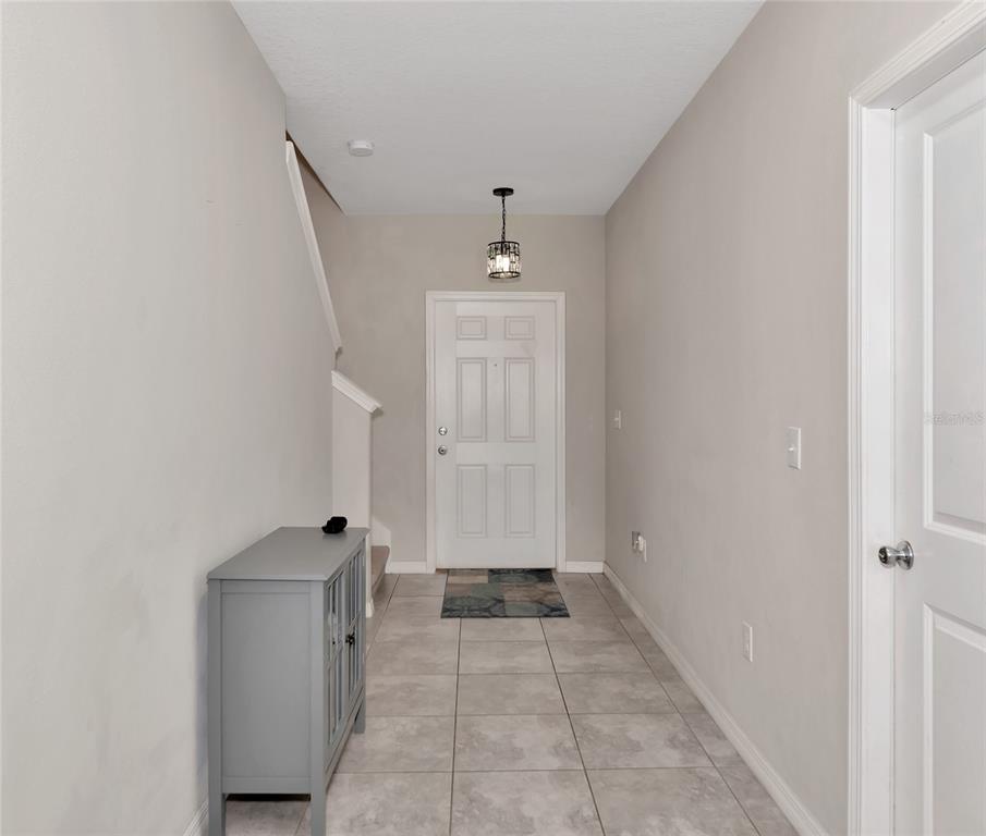 A tiled entryway features a gray cabinet, a staircase, and a white front door — 17009 PEACEFUL VALLEY DRIVE, WIMAUMA, FL