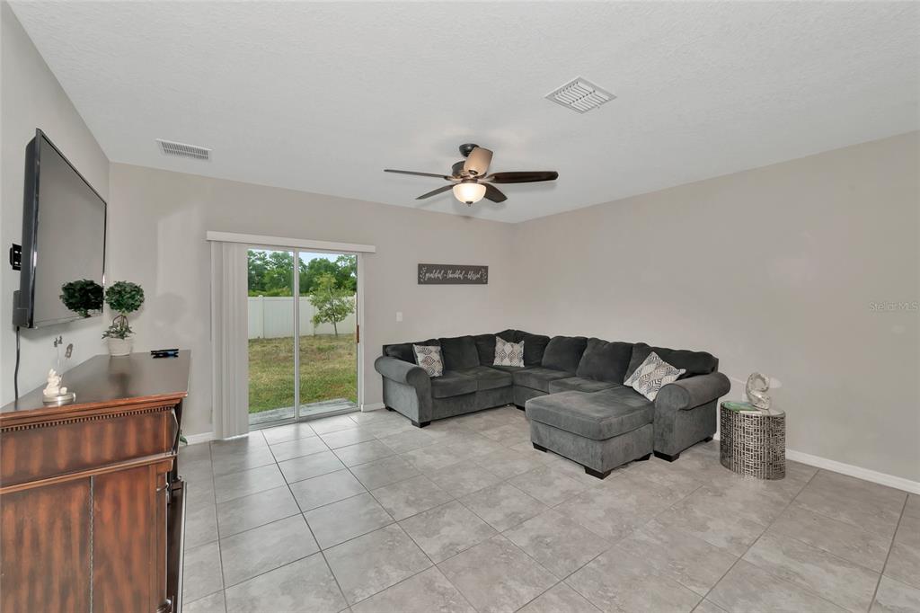 A living room with gray tile floors, a sectional sofa, and a sliding glass door — 17009 PEACEFUL VALLEY DRIVE, WIMAUMA, FL