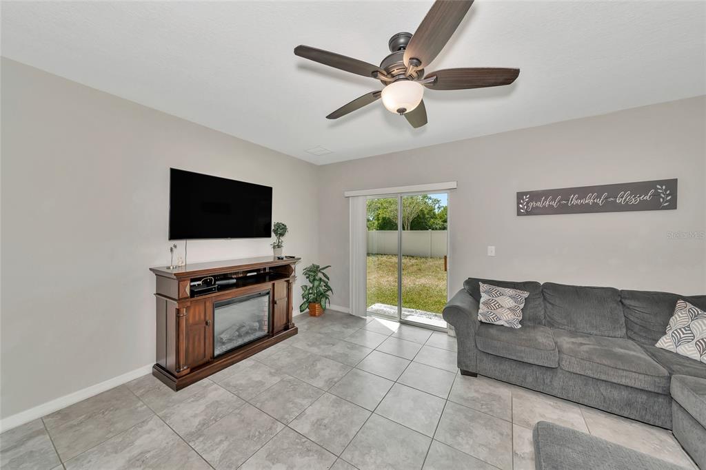 A living room features gray tile flooring, a ceiling fan, a fireplace console, and a sofa — 17009 PEACEFUL VALLEY DRIVE, WIMAUMA, FL