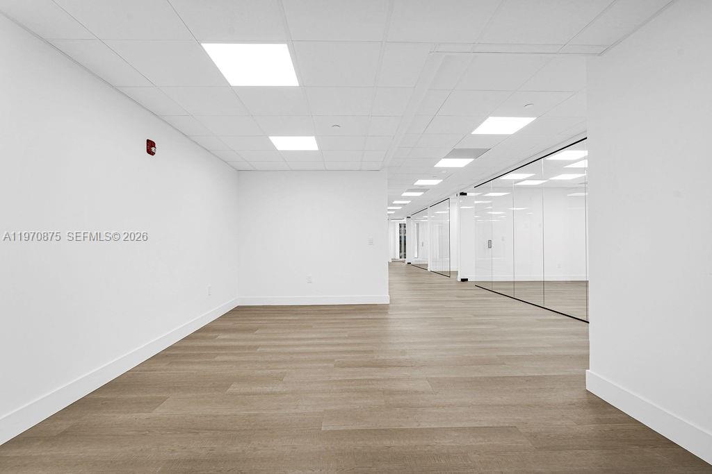 An empty office space features white walls, a drop ceiling, and light wood-look flooring — 1110 Brickell Ave # 310A, Miami FL 33131, MIAMI, FL