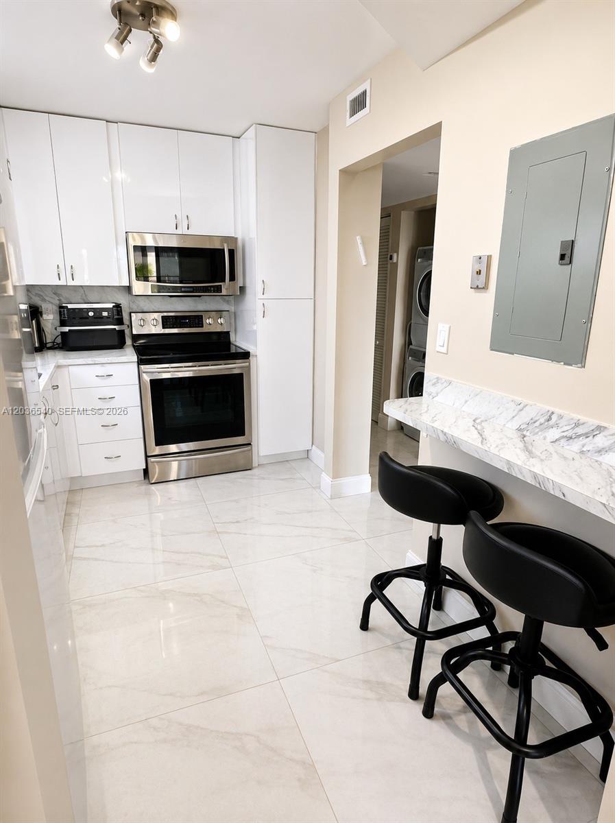 A modern kitchen features white cabinetry, stainless steel appliances, marble countertops, and a breakfast bar — 4122 Collins Ave # 6A, Miami Beach FL 33140, MIAMI BEACH, FL