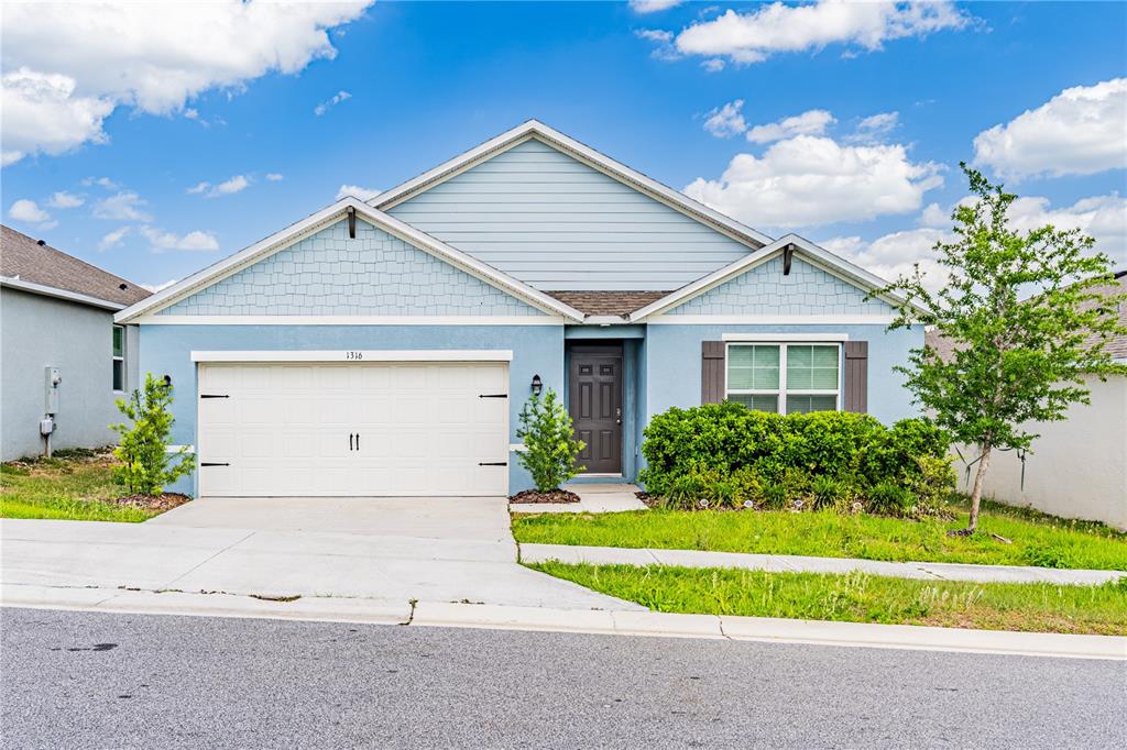 A light blue single-story house features a two-car garage and a front-facing window — 1316 SUGARWOOD STREET, DAVENPORT, FL