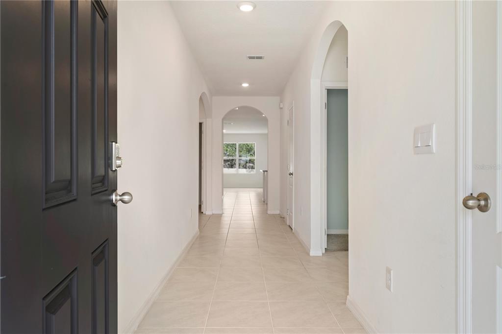 A bright hallway with light tile flooring leads through arched doorways toward a distant window — 1316 SUGARWOOD STREET, DAVENPORT, FL