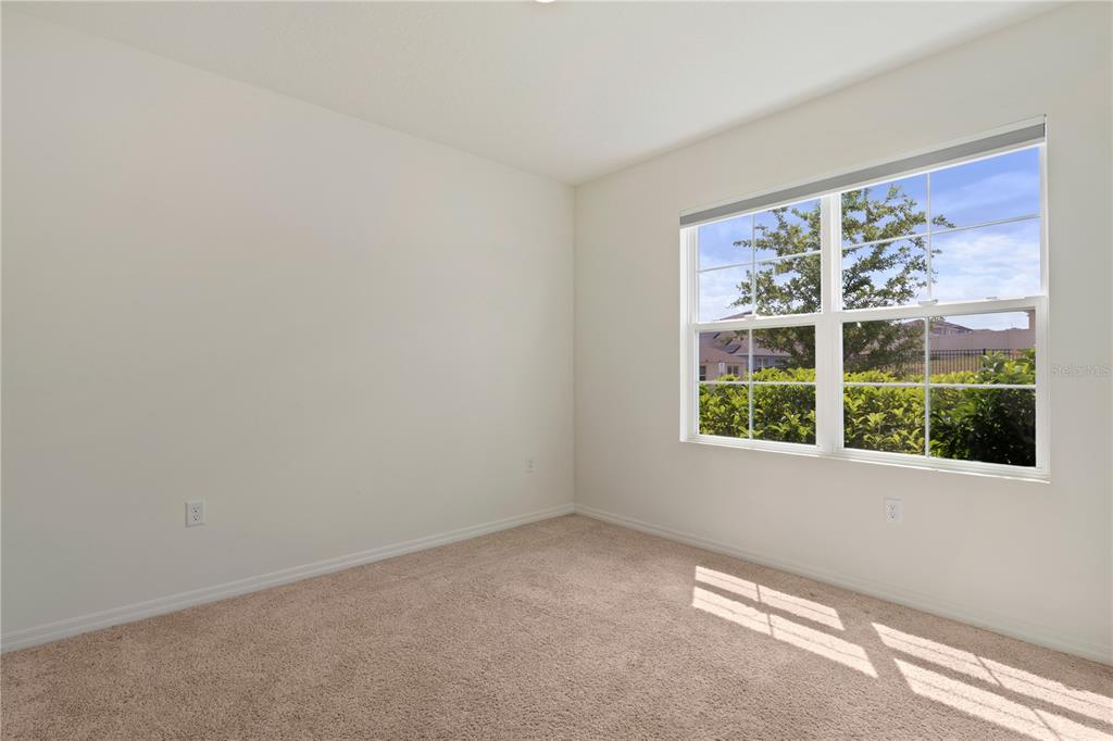 An empty bedroom features beige carpet, white walls, and a window overlooking a green hedge — 1316 SUGARWOOD STREET, DAVENPORT, FL