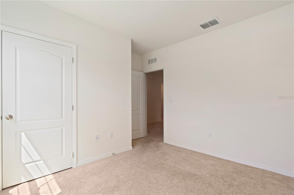 An empty bedroom features beige carpeting, white walls, and two interior doors — 1316 SUGARWOOD STREET, DAVENPORT, FL
