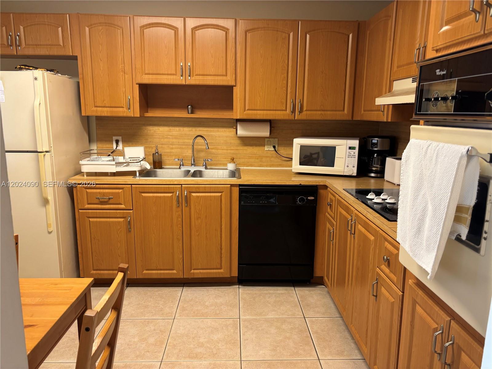 A kitchen features wood cabinets, a double sink, black appliances, and light-colored tile flooring — WESTON, FL