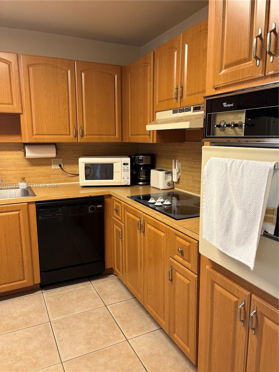 A kitchen features wood cabinets, a black dishwasher, a built-in oven, and tile flooring — WESTON, FL