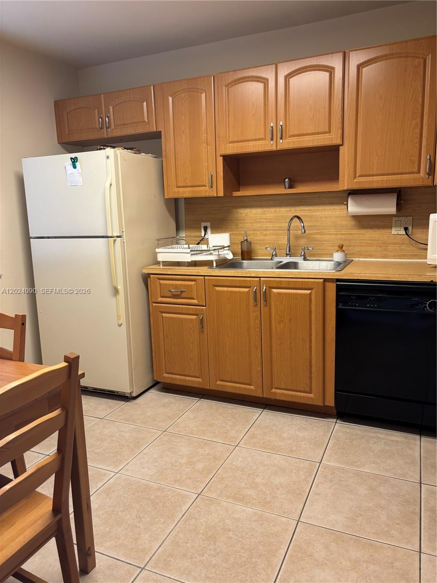 A kitchen features light wood cabinets, a white refrigerator, a black dishwasher, and tiled floors — WESTON, FL
