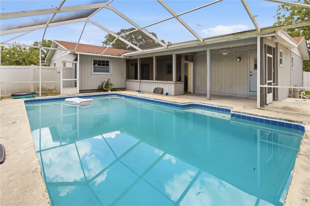 A swimming pool with a screened-in enclosure sits in the backyard of a single-story house — 4921 DETER ROAD, LAKELAND, FL