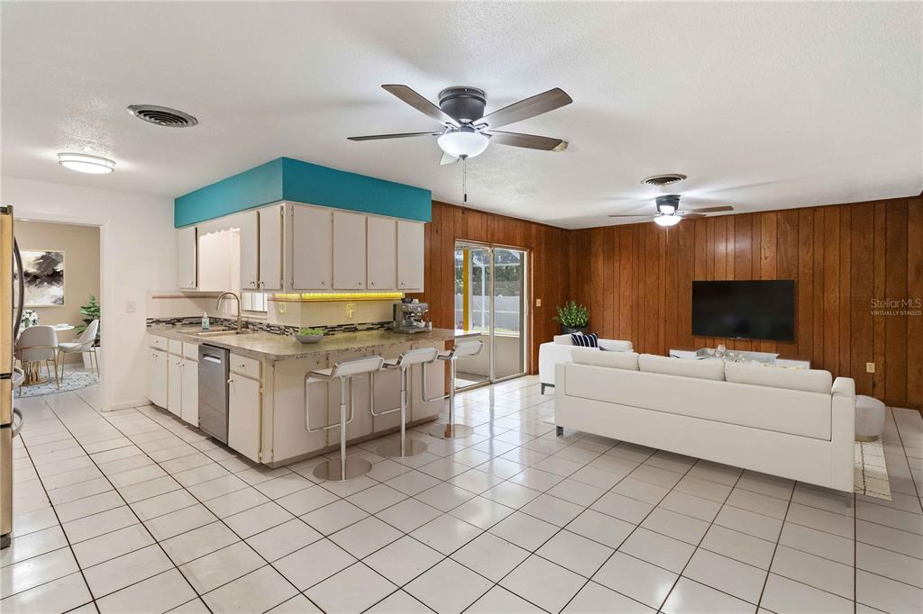 An open-concept living room and kitchen featuring wood-paneled walls, white tile flooring, and bar seating — 4921 DETER ROAD, LAKELAND, FL