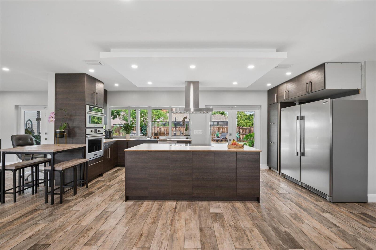 A modern kitchen features dark wood cabinetry, a large central island, and wood-look tile flooring — 4601 W Hawthorne Circle, Hollywood FL 33021, HOLLYWOOD, FL