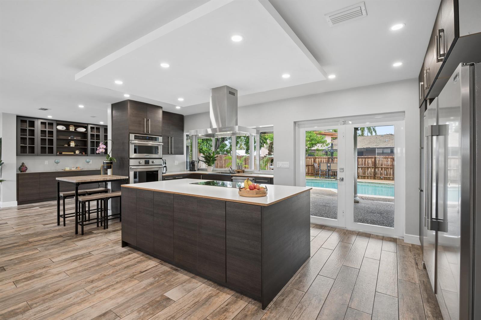 A modern kitchen features dark wood cabinetry, a large central island, and a backyard pool view — 4601 W Hawthorne Circle, Hollywood FL 33021, HOLLYWOOD, FL
