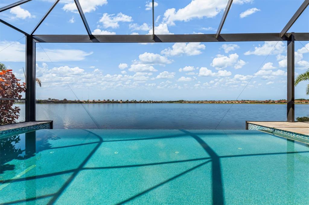 An infinity pool overlooks a large lake from inside a screened-in patio enclosure — 553 MARAVIYA BOULEVARD, NOKOMIS, FL