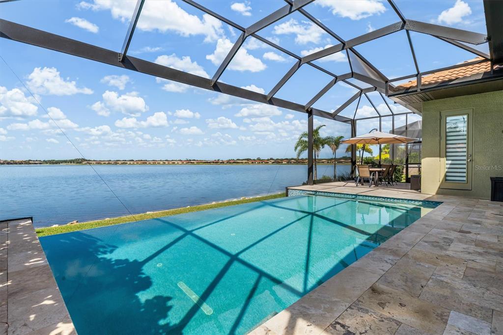 A screened-in patio features a swimming pool overlooking a large lake under a blue sky — 553 MARAVIYA BOULEVARD, NOKOMIS, FL