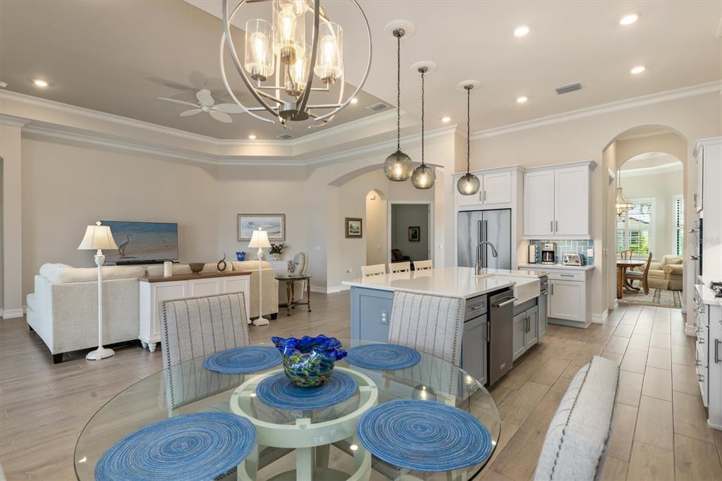 An open-concept kitchen and living area features a glass dining table, island, and neutral decor — 553 MARAVIYA BOULEVARD, NOKOMIS, FL