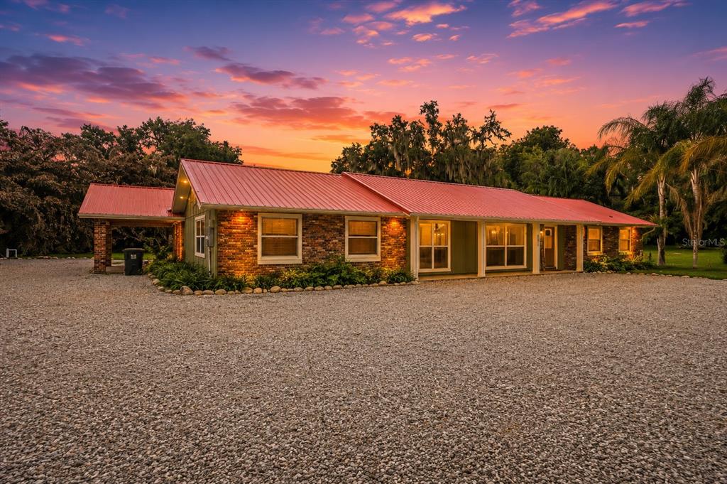 A single-story house with a red metal roof and brick exterior sits on a gravel lot — 2072 LAKE ARIANA BOULEVARD, AUBURNDALE, FL