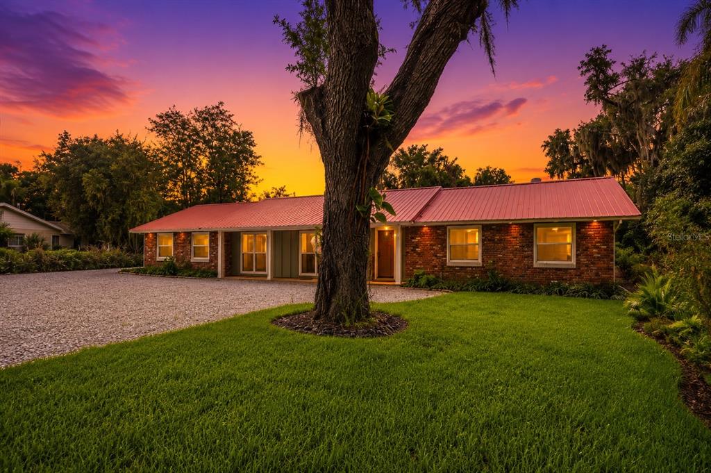 A single-story brick house with a red metal roof stands behind a large tree — 2072 LAKE ARIANA BOULEVARD, AUBURNDALE, FL