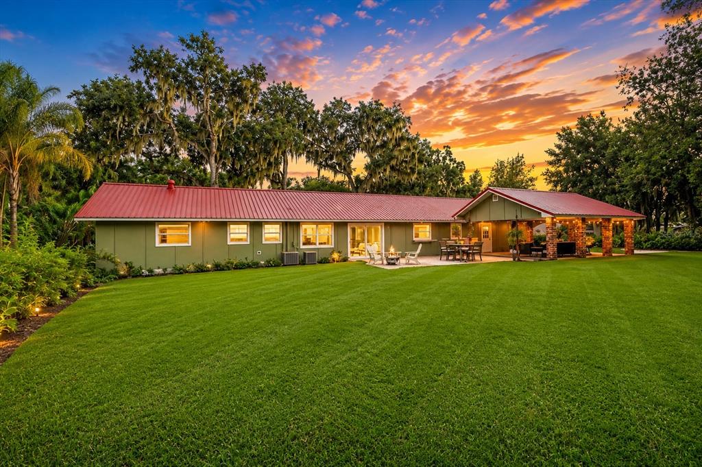 A one-story green house with a red metal roof features a large backyard lawn — 2072 LAKE ARIANA BOULEVARD, AUBURNDALE, FL