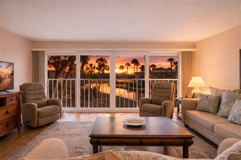 A living room features a large sliding glass door overlooking a sunset over a canal — 6750 GULF OF MEXICO DRIVE UNIT 152, LONGBOAT KEY, FL