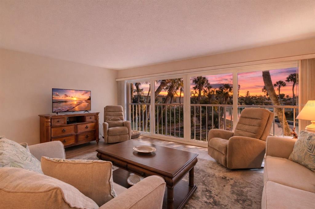 A living room features a wooden coffee table, two recliners, and large windows overlooking sunset — 6750 GULF OF MEXICO DRIVE UNIT 152, LONGBOAT KEY, FL