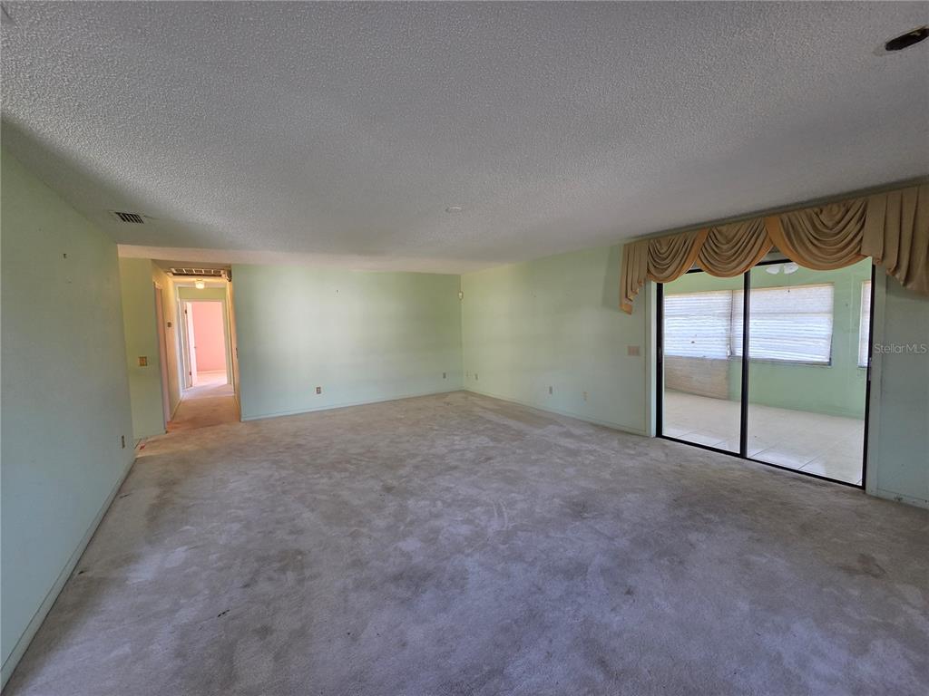 A spacious living room features light green walls, beige carpeting, and sliding glass doors — 842 OSCEOLA AVE, LAKE WALES, FL