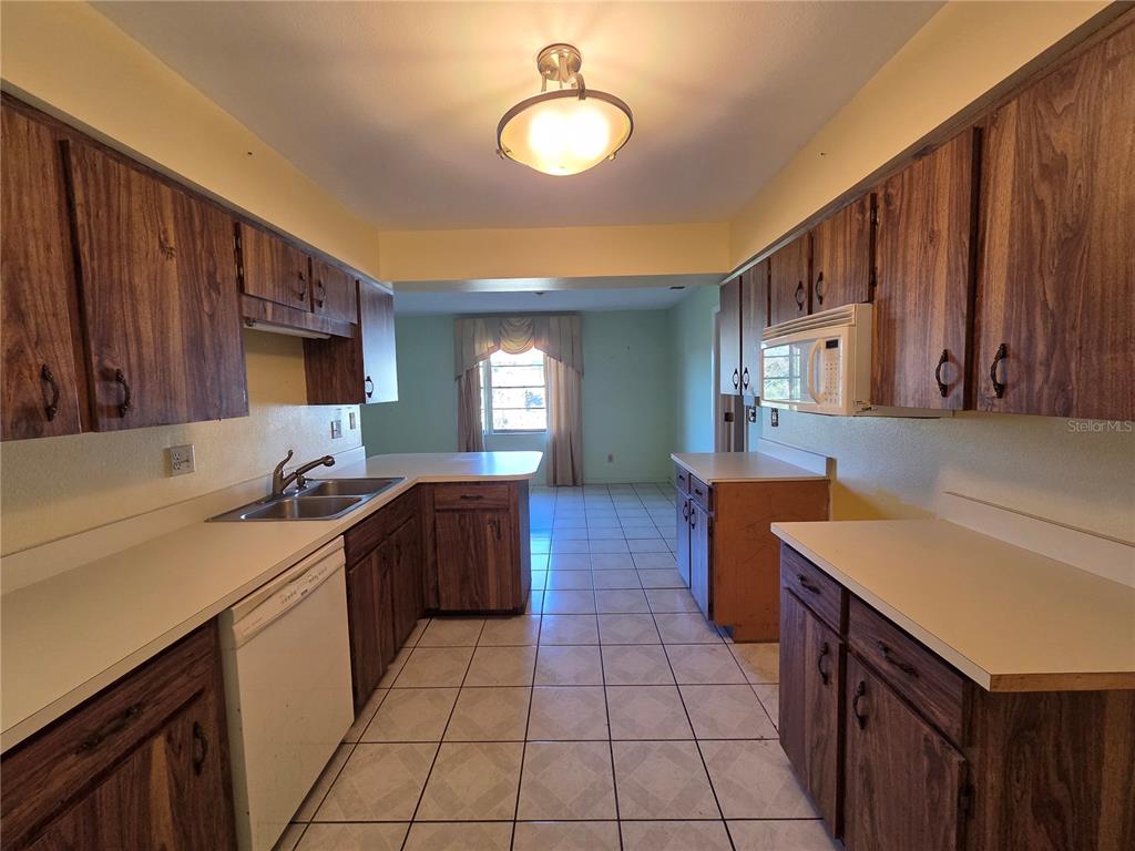 A kitchen features wood cabinets, white countertops, tile flooring, and a white dishwasher — 842 OSCEOLA AVE, LAKE WALES, FL