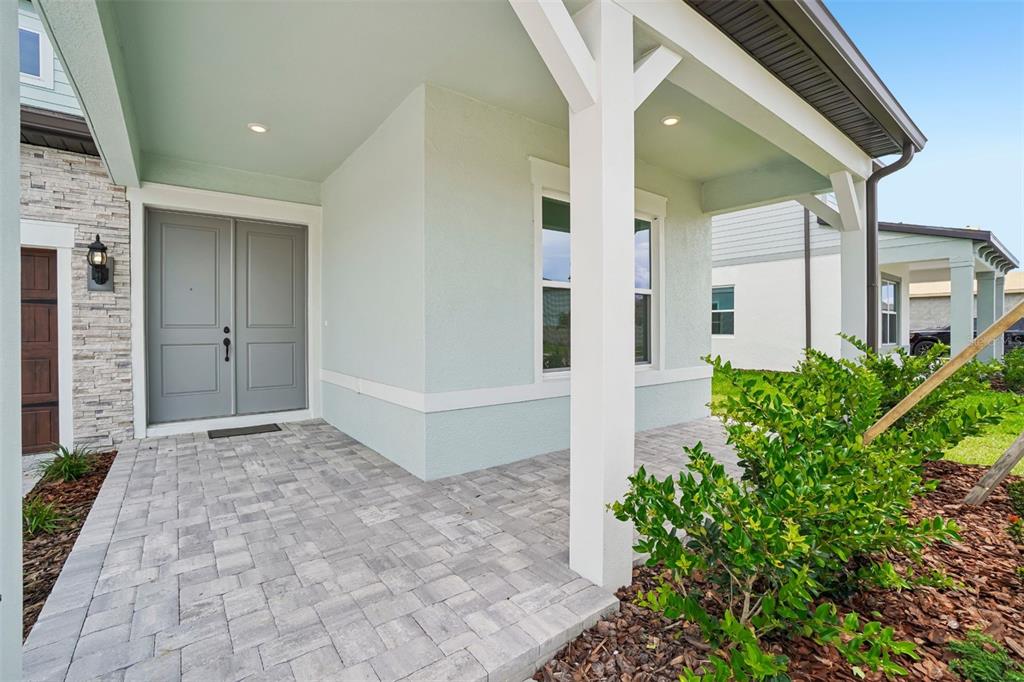 A covered front porch features gray double doors, stone siding, and light-colored stucco walls — 34931 BLAINE PASS, ZEPHYRHILLS, FL