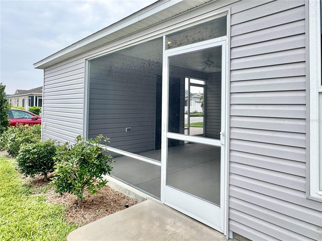 A screened-in porch with a white door is attached to the side of a house — 6316 WHITTLE COURT, THE VILLAGES, FL