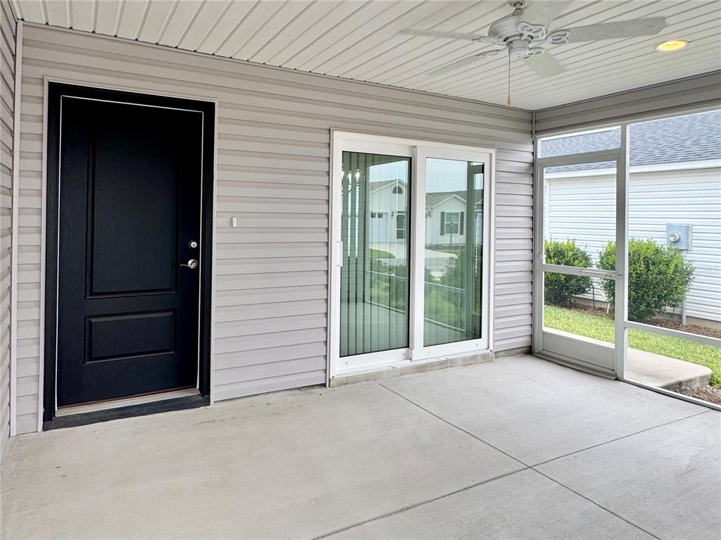 A covered patio features a black door, sliding glass doors, and a screened-in wall — 6316 WHITTLE COURT, THE VILLAGES, FL