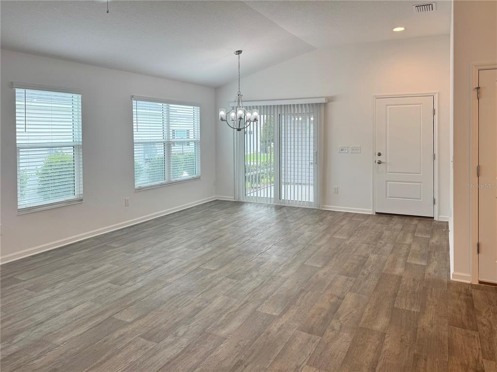 An empty dining area features wood-look flooring, a chandelier, two windows, and a sliding door — 6316 WHITTLE COURT, THE VILLAGES, FL