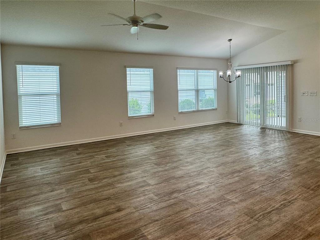 A spacious living area features light-colored walls, wood-look flooring, a ceiling fan, and sliding doors — 6316 WHITTLE COURT, THE VILLAGES, FL