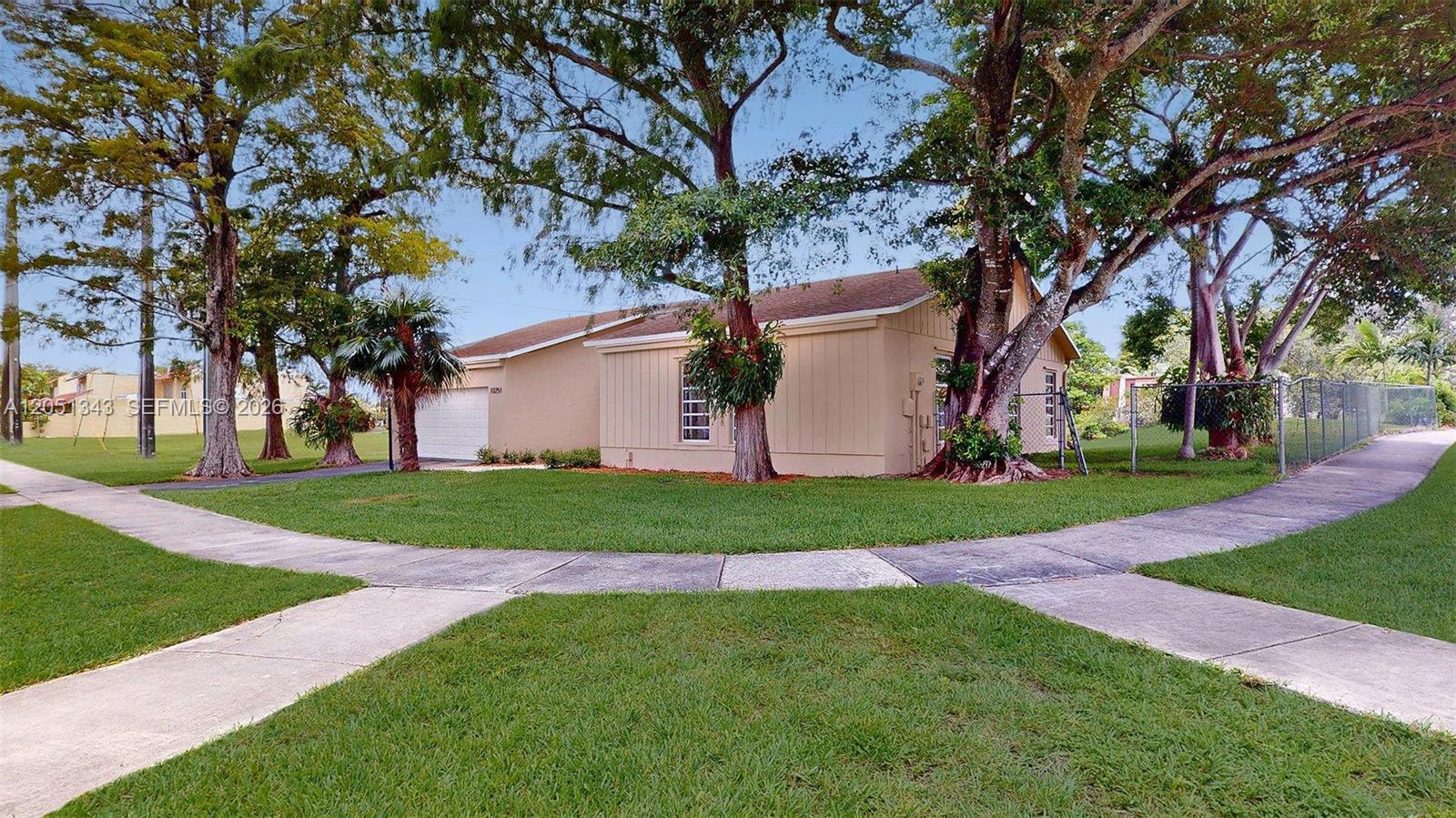 A single-story house with tan siding and a garage sits behind a grassy lawn — 10251 SW 80th St # 0, Miami FL 33173, MIAMI, FL