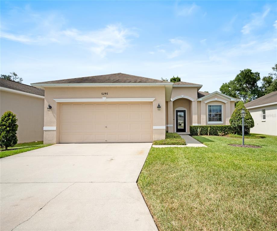 A single-story house with a tan stucco exterior, a two-car garage, and a front lawn — 6246 SILVER LEAF LANE, LAKELAND, FL