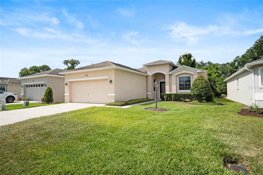 A single-story suburban house with a tan stucco exterior, a two-car garage, and a lawn — 6246 SILVER LEAF LANE, LAKELAND, FL