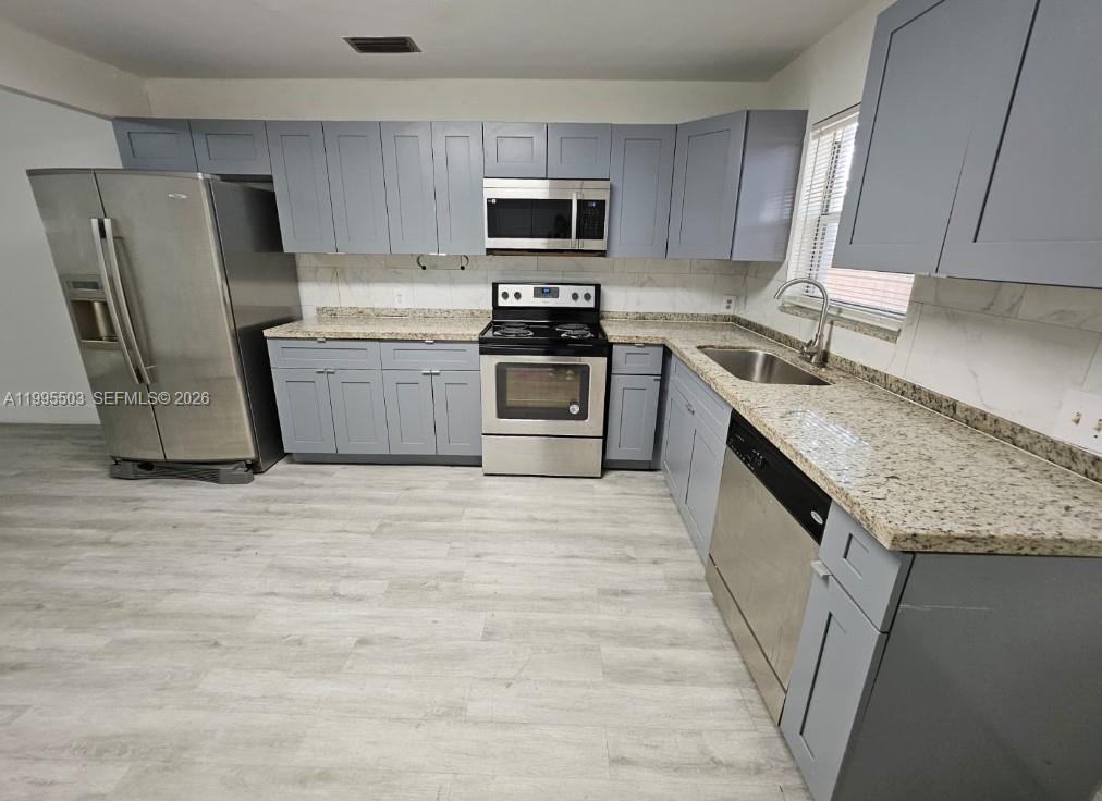A kitchen features gray cabinets, stainless steel appliances, and granite countertops over light wood flooring — 209 SW 9th St # 209, Hallandale Beach FL 33009, HALLANDALE BEACH, FL