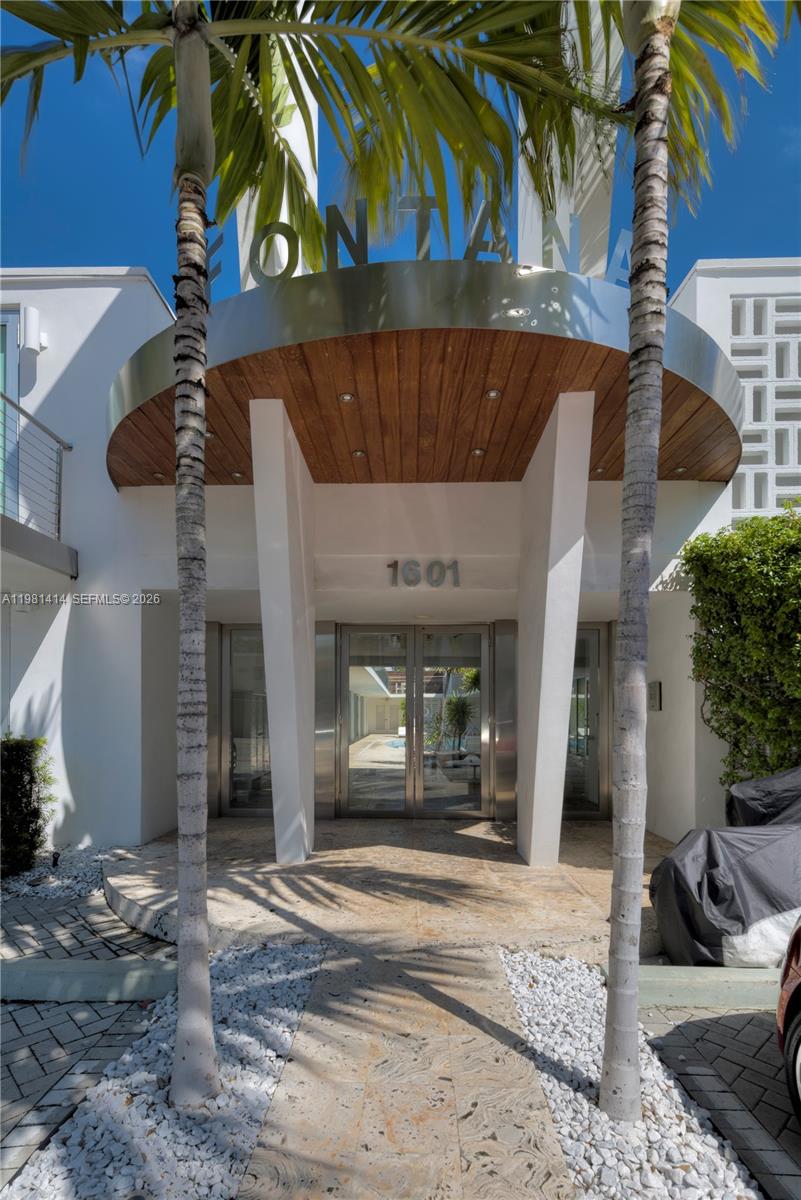 The exterior entrance of a building features a curved wooden canopy and two palm trees — 1601 West Ave # 202, Miami Beach FL 33139, MIAMI BEACH, FL