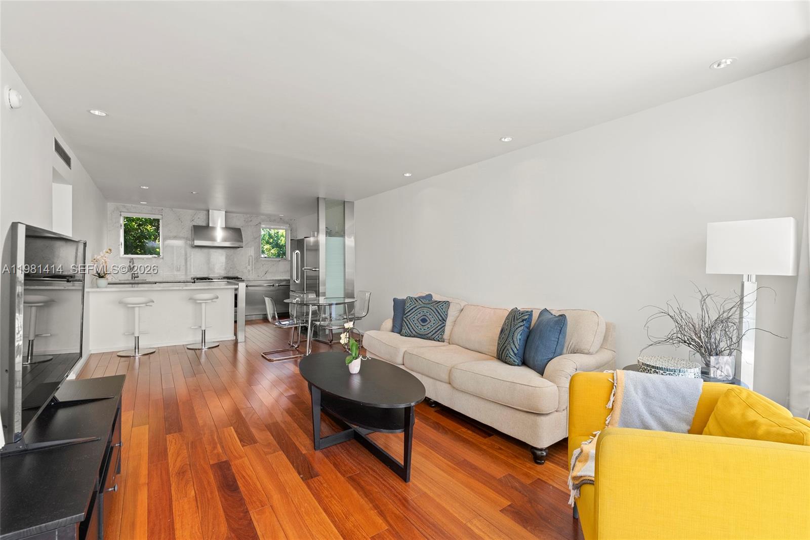 A living room with hardwood floors features a beige sofa, yellow armchair, and open kitchen — 1601 West Ave # 202, Miami Beach FL 33139, MIAMI BEACH, FL