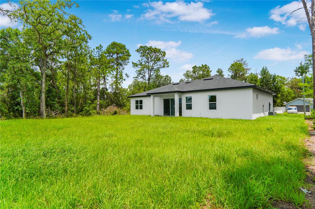 The rear exterior of a white single-story house sits behind a large, grassy field — 5220 SW 128TH PLACE, OCALA, FL