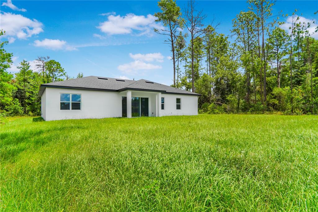 The rear exterior of a white single-story house sits behind a large, grassy field — 5220 SW 128TH PLACE, OCALA, FL