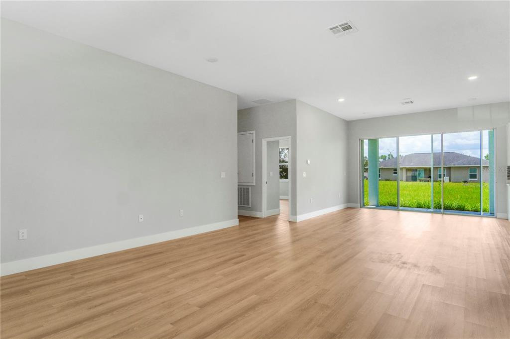 An empty room with light wood-look flooring, gray walls, and large sliding glass doors — 5220 SW 128TH PLACE, OCALA, FL