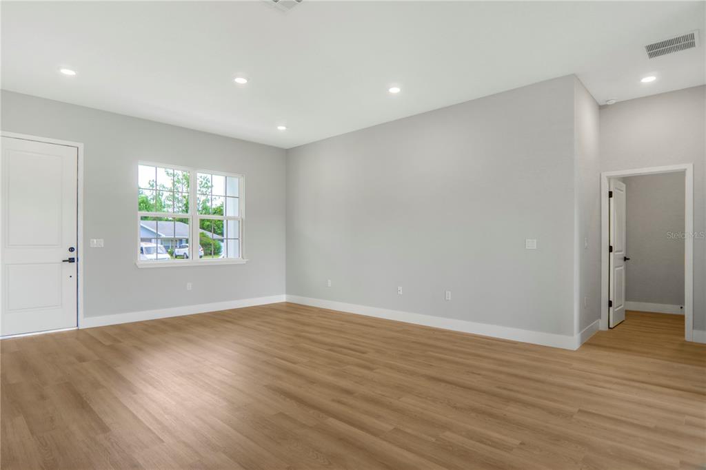 An empty room features light gray walls, wood-look flooring, recessed lighting, and a window — 5220 SW 128TH PLACE, OCALA, FL