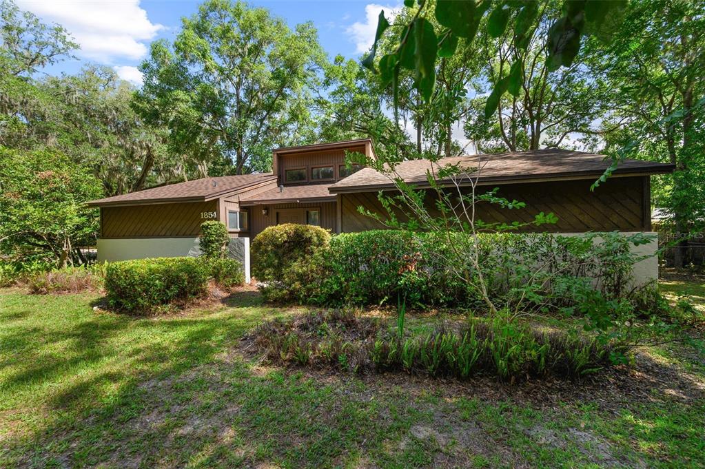 A single-story house with brown wood siding and a raised roof section sits among trees — 1854 NW 41ST PLACE, GAINESVILLE, FL