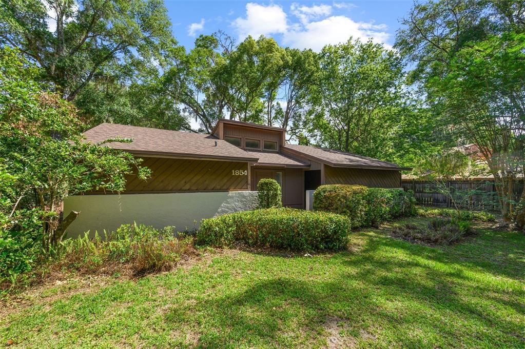 A single-story house with brown wood siding and a white stucco base sits among trees — 1854 NW 41ST PLACE, GAINESVILLE, FL