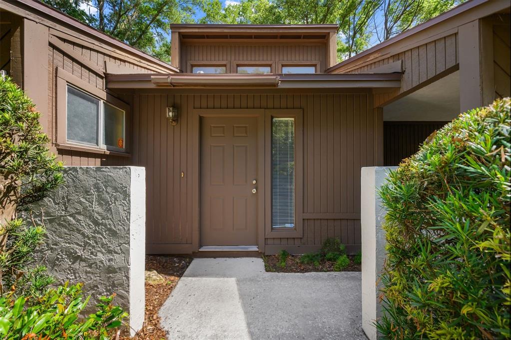 The exterior of a brown house features a front door, vertical siding, and concrete walkway — 1854 NW 41ST PLACE, GAINESVILLE, FL