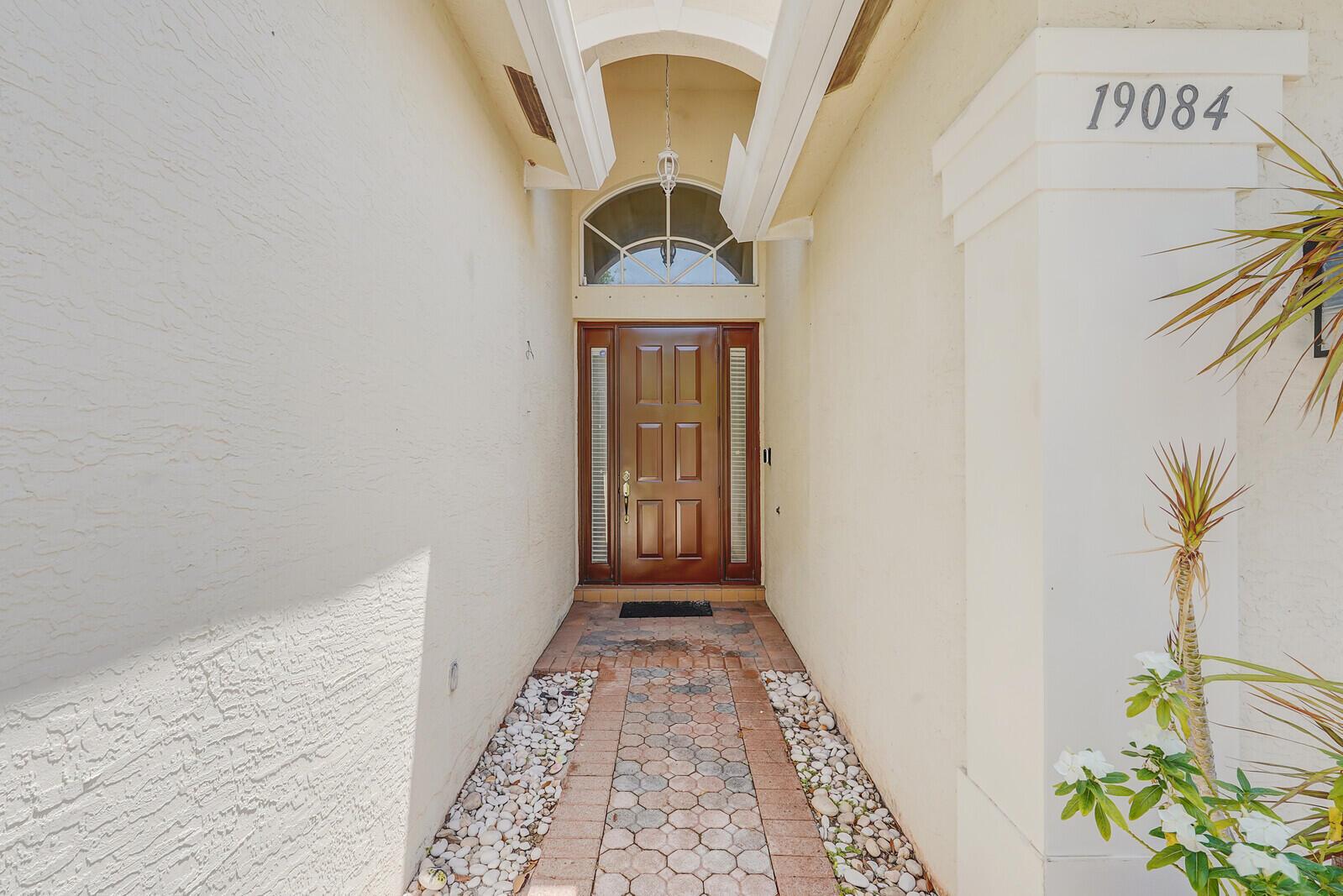 A front entryway features a wooden door with sidelights, a stone path, and stucco walls — 19084 Skyridge Circle, Boca Raton FL 33498, BOCA RATON, FL